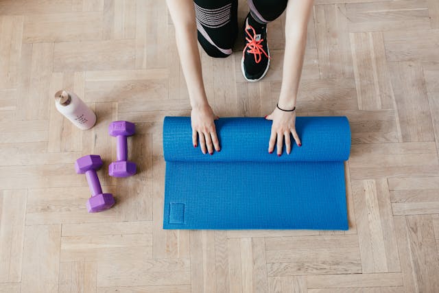 An athlete unfolds her exercise mat on a wooden floor, ready to practice her healthy eating and exercise habits.